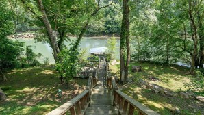 Eine Holzbrücke führt zu einer Hütte am See, der von Bäumen umgeben ist.