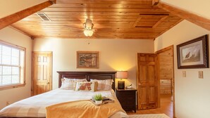 Ein Schlafzimmer mit Holzboden, einem Bett mit weißer und beiger Bettdecke, einem Nachttisch mit Lampe und einem gerahmten Bild an der Wand.