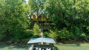 Ein schwimmendes Haus mit einer Terrasse, einem überdachten Sitzbereich und einer Treppe, die zu einer oberen Ebene führt.