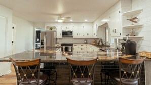 A modern kitchen with white cabinets, a granite island, and three bar stools. - 4 Bedroom + 3.5 Bathroom Greers Ferry Lakefront Home in Heber Springs! (Heber Springs)