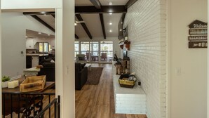 A spacious living area with a kitchen in the background, wooden flooring, and a white brick wall. - 4 Bedroom + 3.5 Bathroom Greers Ferry Lakefront Home in Heber Springs! (Heber Springs)