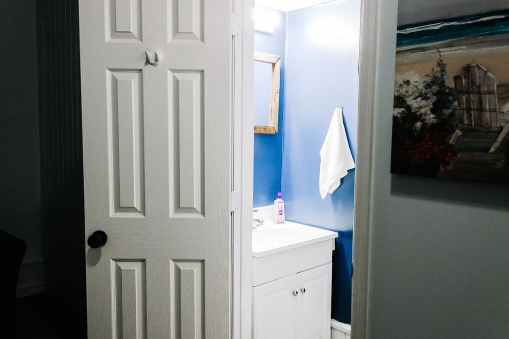 Une salle de bain avec une porte blanche, un mur bleu, un lavabo blanc et un miroir.