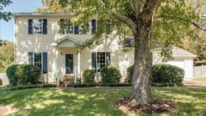 A two-story house with a front porch, a large tree in front, and a well-maintained lawn.
