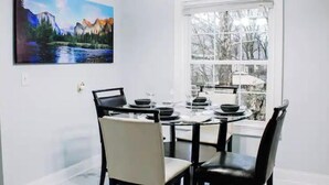 A dining area with a round table, black chairs, and a painting of a mountain landscape.