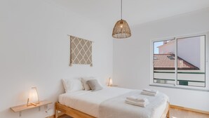 A modern bedroom with a wooden bed, bedside lamps, a hanging light fixture, a view of the outside, and a wall-mounted artwork. - Alta do Garajau I (Santa Cruz)