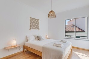 Un dormitorio moderno con cama de madera, lámparas de noche, lámpara colgante, ventana con vistas y un adorno en la pared.