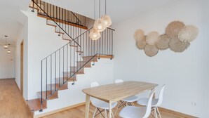 A modern interior with a wooden staircase, a dining table with chairs, and decorative wall art. - Alta do Garajau I (Santa Cruz)