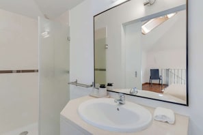Ein modernes Badezimmer mit einem großen Spiegel, einem Waschbecken und einer Duschkabine aus Glas.