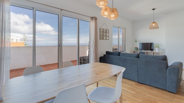 A modern living room with a dining area, large windows, and a flat-screen TV. - Alta do Garajau I (Santa Cruz)