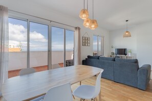 Een moderne woonkamer met een eethoek, grote ramen en een flatscreen televisie.