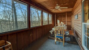 Eine Hütte mit Holzvertäfelung, großen Fenstern, einem Deckenventilator und einem Tisch mit Stühlen.