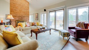 A spacious living room with a brick wall, a chandelier, and large windows offering a view of the outdoors. - Peaceful Millington Home ~ 13 Mi to Memphis! (Millington)
