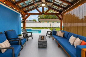 Een overdekte terras met blauwe banken, stoelen en een vuurkorf.