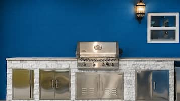 A barbecue grill with a stainless steel finish, a stone countertop, and a blue wall in the background.