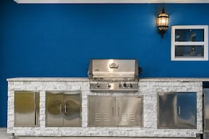 A barbecue grill with a stainless steel finish, a stone countertop, and a blue wall in the background. - 2 Homes- Heated Pool & Pickleball- The Dunedin Duo (Dunedin, Florida)