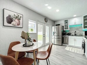 Een moderne keuken met roestvrijstalen apparatuur, een eethoek met een witte tafel en bruine stoelen, en een lijstwerk met kunst aan de muur.