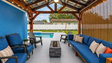 An outdoor patio with a pool, blue furniture, and a pergola with string lights.