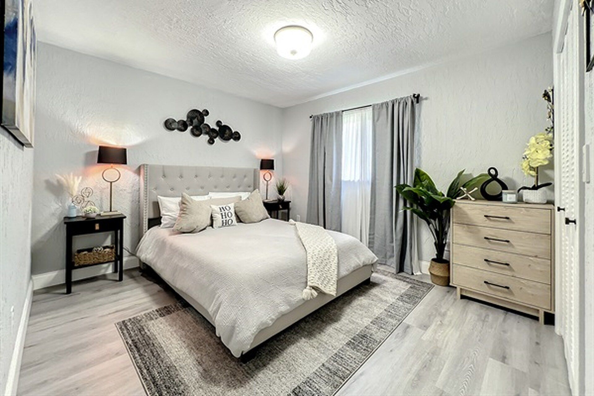 A modern bedroom with a large bed, bedside lamps, a dresser, and a potted plant.