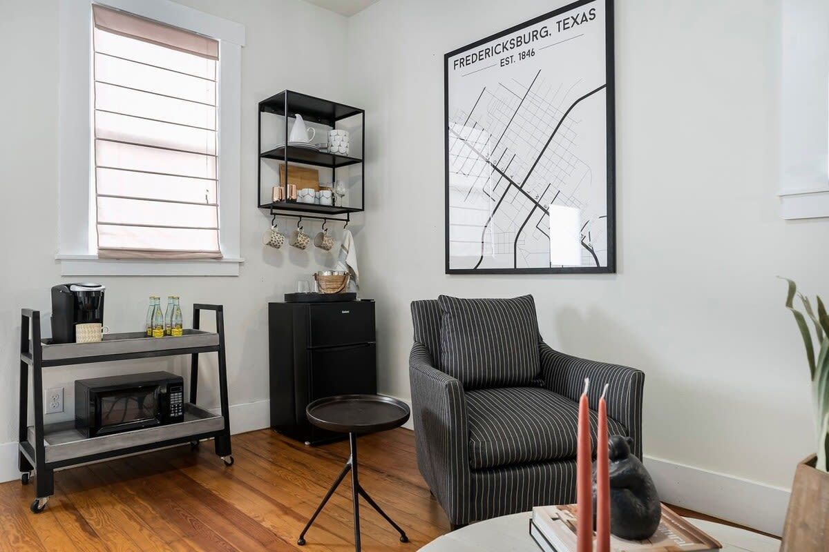 A modern living room with a black-framed sofa, a coffee table, a black cart with a microwave, a small side table, and a wall-mounted shelf with decorative items.