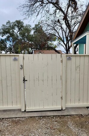 A white wooden gate with a number '3' on it, leading to a house with a green roof. - The Downtown Studio 3, Hot tub, Cowboy Pool! (Fredericksburg)