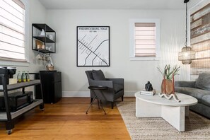 A modern living room with a map of Fredericksburg, Texas, a black shelving unit, a striped armchair, a white coffee table, and a grey sofa. - The Downtown Studio 3, Hot tub, Cowboy Pool! (Fredericksburg)