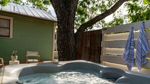 Ein Whirlpool in einem Garten mit einem Baum, einem Holzzaun und einem grünen Haus im Hintergrund.