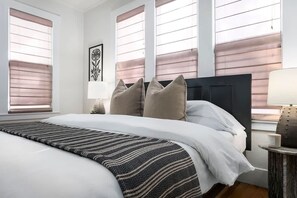 A hotel room with a large bed, two bedside tables, a window with blinds, and a framed picture on the wall. - The Downtown Studio 3, Hot tub, Cowboy Pool! (Fredericksburg)