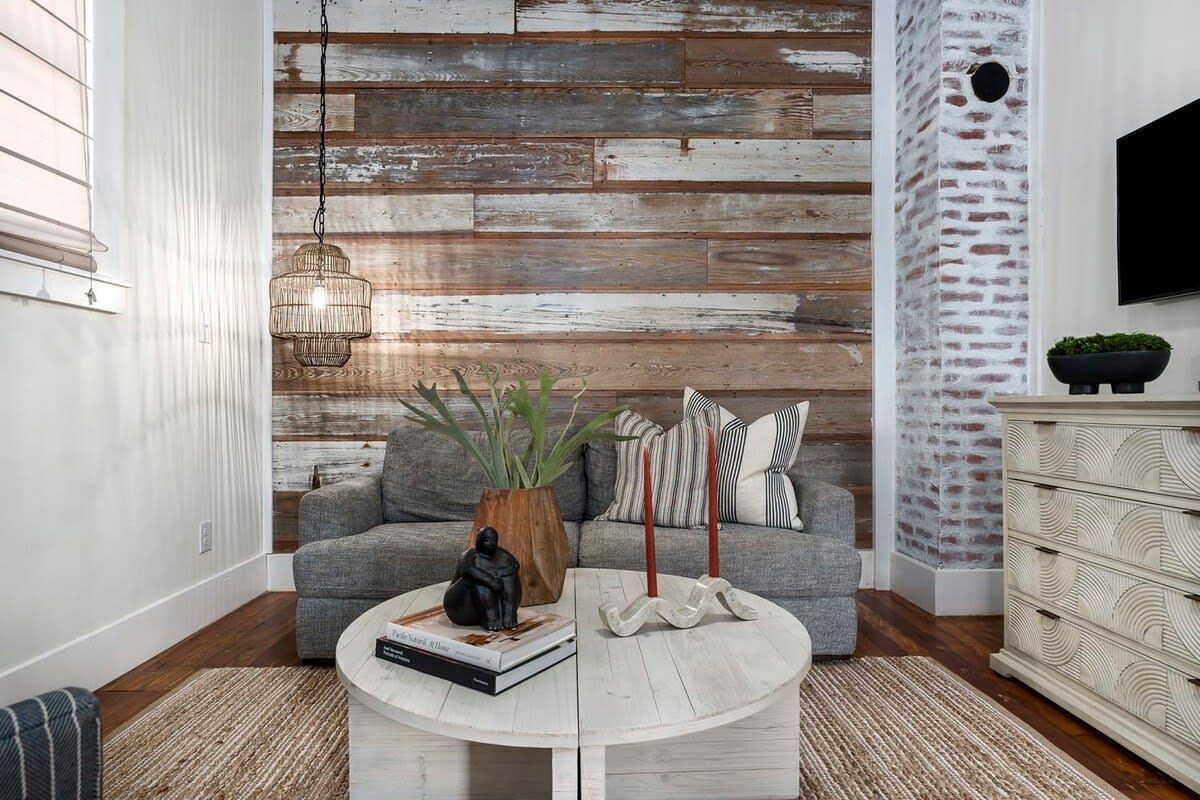 A living room with a grey sofa, a round coffee table, a hanging light fixture, and a brick-patterned wall.