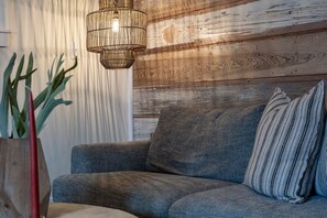 A living room with a grey sofa, a striped pillow, a hanging light fixture, and a plant in a wooden vase. - The Downtown Studio 3, Hot tub, Cowboy Pool! (Fredericksburg)