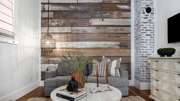 Ein Wohnzimmer mit einem grauen Sofa, einem runden Couchtisch und einer rustikalen Holzwand.