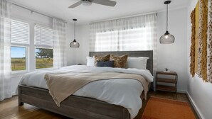 Een slaapkamer met een bed, nachtkastje, plafondventilator en een raam met uitzicht.