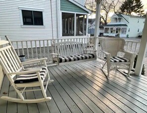 Een houten terras met schommelstoelen en een bank, met uitzicht op een woonwijk.