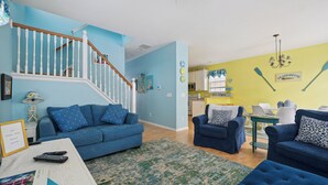 A living room with blue sofas, a staircase, and a kitchen area with yellow walls. - Beautiful home in Chautauqua community - linens, parking, washer Included (Lakeside Marblehead)