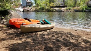Orilla de río con kayaks y una casa al fondo.