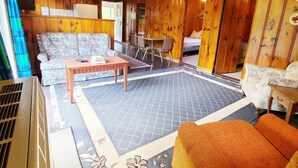 A cozy room with wooden walls, a sofa, a small table, a bed, and a ceiling fan. - The Fisherman - 3-bedroom River-front Retreat (Selwyn)