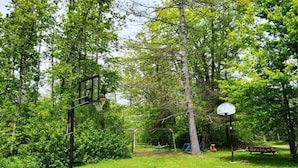 A basketball court with a hoop, a picnic table, and a swing set in a park. - The Fisherman - 3-bedroom River-front Retreat (Selwyn)