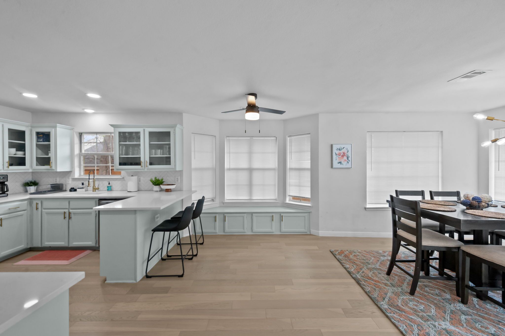 Une cuisine moderne avec des meubles blancs, un îlot central et un coin repas comprenant une table et des chaises.