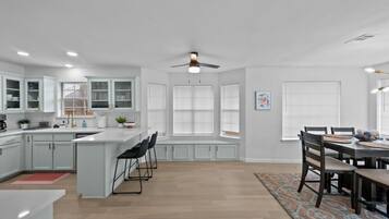 Une cuisine moderne avec des meubles blancs, un îlot central et un coin repas comprenant une table et des chaises.
