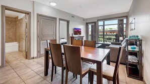 A modern dining area with a wooden table and chairs, a TV, and a view of the outdoors. - Playa Del Sol Retreat 550 | Pool + Hot Tub | (Kelowna)