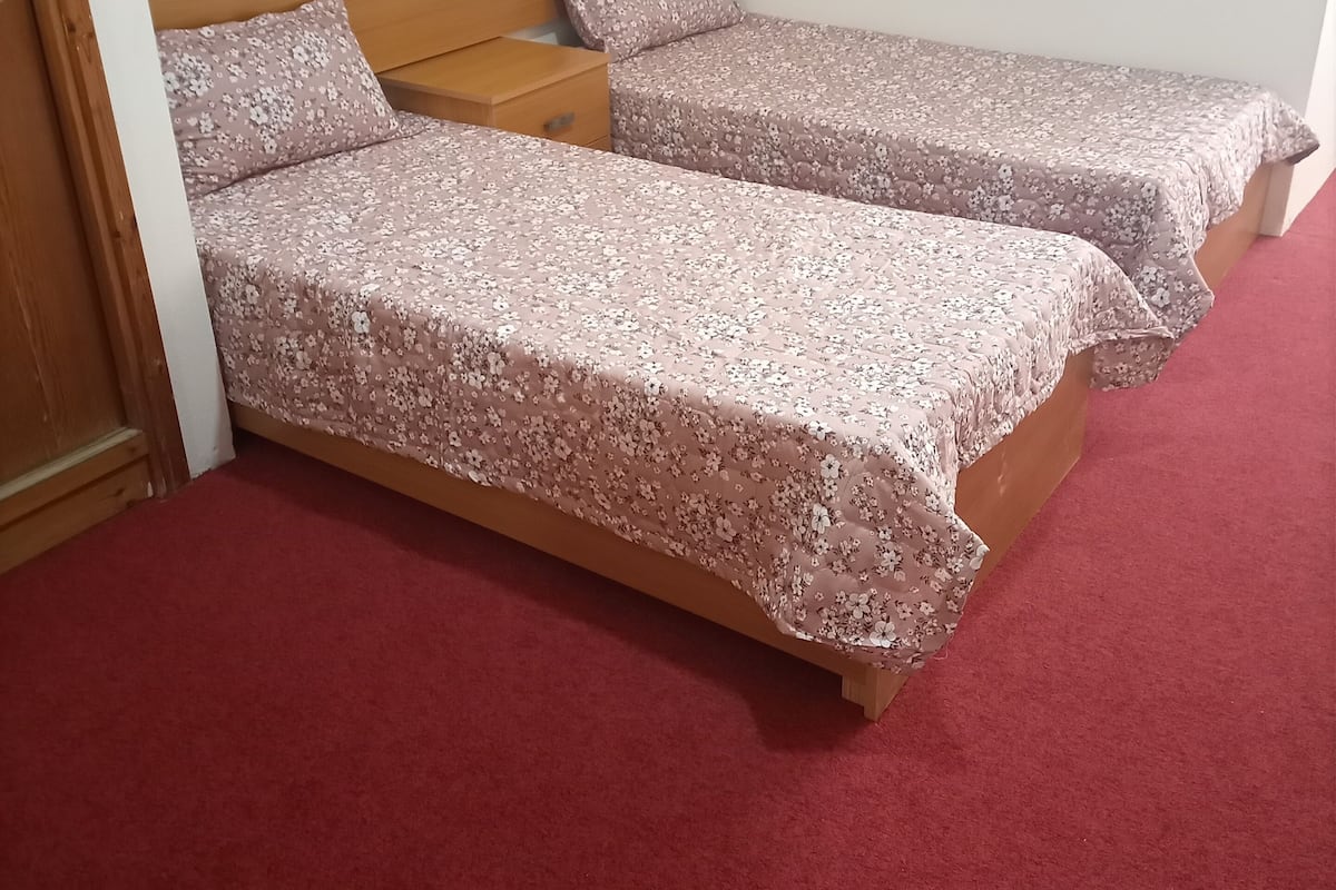 A room with two single beds, each with a wooden headboard and floral bedding.