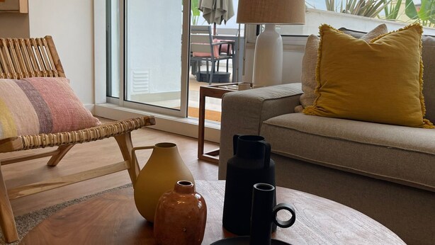 A modern living room with a wooden coffee table, a sofa with a yellow pillow, and a large window offering a view of the outdoors. - Apart 3Bdr with River view and private Patio - Center of Lisbon (Lisboa)