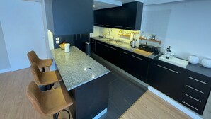 A modern kitchen with dark cabinetry, a granite countertop, and a built-in oven. There are two bar stools and a small island with a sink. - Apart 3Bdr with River view and private Patio - Center of Lisbon (Lisboa)