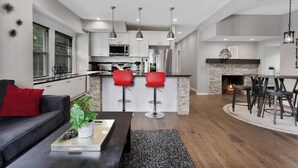 A modern kitchen with white cabinets, a central island with red bar stools, and a dining area with a fireplace. - Spacious 5 Bedroom Duplex In Kansas City! 65/66 (Kansas City)