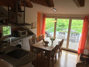 A kitchen with a microwave, toaster, and sink. There is a dining table with chairs and a vase of flowers. The room has a large sliding glass door leading to a deck with outdoor furniture. - Feel-good top-floor apartment with terrace, whirlpool, fireplace - Apartment B (Neuenweg/Kleines Wiesental)