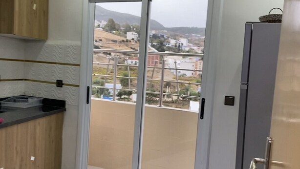 A modern kitchen with a large sliding glass door leading to a balcony, a wooden cabinet, and a grey utility cabinet. - Casa. Aziz (Chefchaouen)