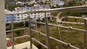 A balcony with a metal railing overlooking a hillside with buildings. - Casa. Aziz (Chefchaouen)