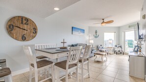 A dining area with a wooden clock, white chairs, a table, and a ceiling fan.