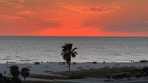 A beach with people walking, palm trees, and a sunset over the ocean.