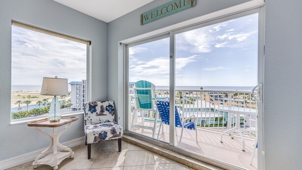 A balcony with a "WELCOME" sign, a table with a lamp, and a floral chair.