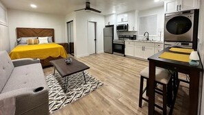 A compact hotel room with a bed, a sofa, a dining table, a kitchen area with appliances, and a ceiling fan. - Airy Arty Studio with Amenities (Gardena)